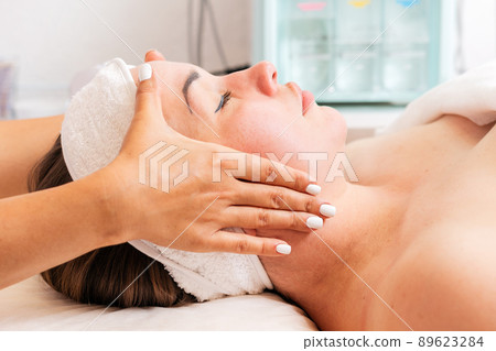 A cosmetologist makes a facial massage procedure for a woman. Close-up of the client's face. Concept of cosmetology and treatment A cosmetologist makes a facial massage procedure for a woman. Close-up of the client's face. Concept of cosmetology and treatment 89623284