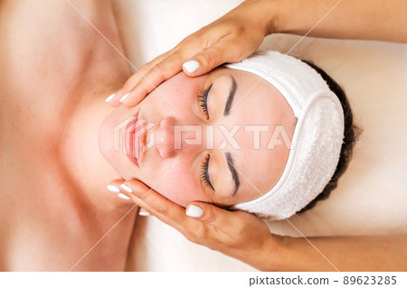 Cosmetologist makes a woman a facial massage procedure. Portrait of the client and the doctor's hands in close-up. The view from the top. Concept of cosmetology and treatment 89623285