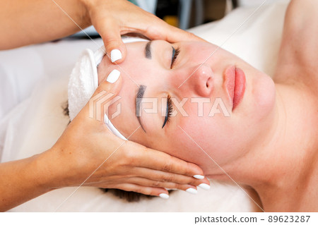 Cosmetologist massages the woman's face. Portrait of the client and the doctor's hands in close-up. The view from the top. Concept of cosmetology and treatment Cosmetologist massages the woman's face. Portrait of the client and the doctor's hands in close-up. The view from the top. Concept of cosmetology and treatment 89623287