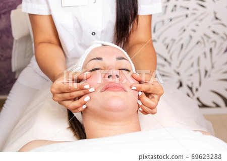 Cosmetologist massages the woman's face, smoothing out wrinkles. Portrait of the client and the doctor's hands in close-up. Concept of cosmetology and treatment 89623288