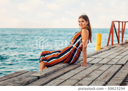 Portrait of a young, pretty woman was leaning against the wooden pier. In the background the sea. Concept of summer holiday. Copy space Portrait of a young, pretty woman was leaning against the wooden pier. In the background the sea. Concept of summer holiday. Copy space 89623294