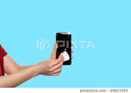 Disinfection. A woman wipes the smarfton with an antibacterial cloth. Blue background. Copy space. The concept of protection from the virus and disinfection 89623364