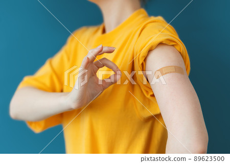 Girl at yellow t-shirt shows a hand with a band-aid stuck on it, shows a gesture OK. Dark blue background. The concept of immunization and coronavirus vaccination 89623500