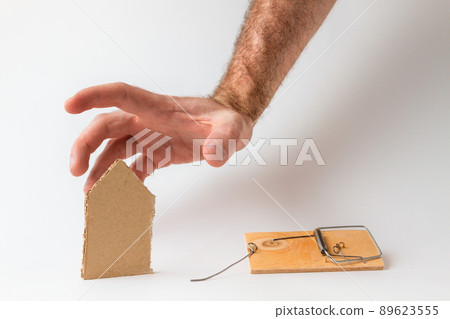 Bank investments and mortgages. Male hand reaching for the cardboard house, lying next to the trap.White background. Copy space 89623555