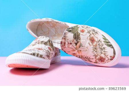 Pair of female's new stylish slip-ons with floral ornament on a pink-blue background. Close up Pair of female's new stylish slip-ons with floral ornament on a pink-blue background. Close up 89623569