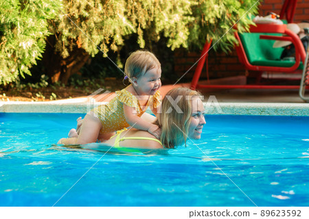 Teaching to swimming. Portrait of happy mother with a little baby girl swimming in the pool. Copy space. Summer activity 89623592