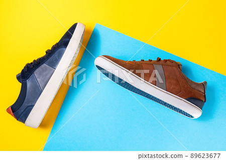 Two man's new stylish sneakers made of blue and brown leather on a yellow-blue background. Flat lay. Copy space. Side view of shoes 89623677