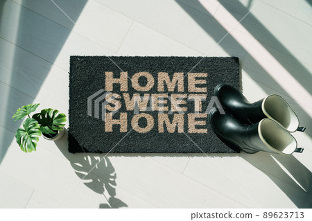 Rain boots on home sweet Home door mat during fall rainy season. Entrance doormat of house homeowner. Top view of rug for floor protection of rain water during autumn. 89623713