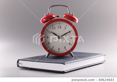 Red retro clock stand on top of closed book or diary, time to study, time to learn new information Red retro clock stand on top of closed book or diary, time to study, time to learn new information 89624683