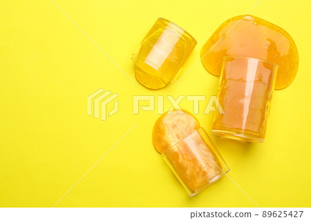 Overturned plastic containers with bright slimes on yellow background, top view. Space for text 89625427