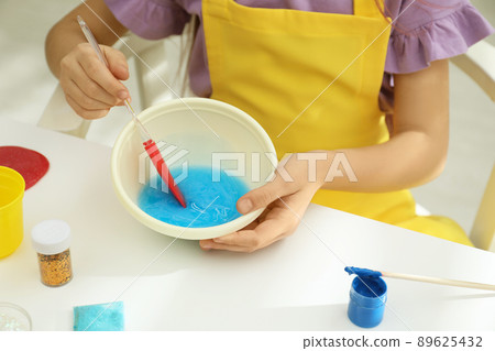 Little girl mixing ingredients with silicone spatula at table, closeup. DIY slime toy Little girl mixing ingredients with silicone spatula at table, closeup. DIY slime toy 89625432