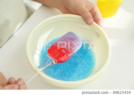 Little girl mixing ingredients with silicone spatula at table, closeup. DIY slime toy Little girl mixing ingredients with silicone spatula at table, closeup. DIY slime toy 89625434