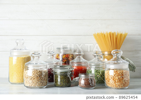 Glass jars with different types of groats and pasta on white wooden table Glass jars with different types of groats and pasta on white wooden table 89625454