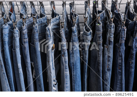 Rack with stylish jeans near brick wall, closeup 89625491