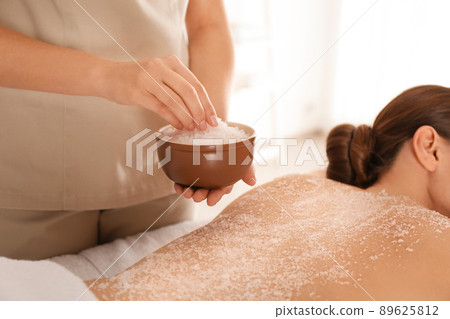 Young woman having body scrubbing procedure with sea salt in spa salon, closeup 89625812