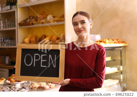 Female business owner holding OPEN sign in bakery Female business owner holding OPEN sign in bakery 89625822