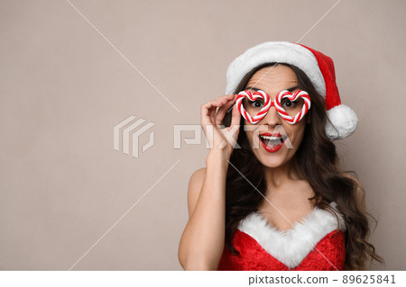 Emotional woman in Christmas costume with party glasses on beige background, space for text Emotional woman in Christmas costume with party glasses on beige background, space for text 89625841
