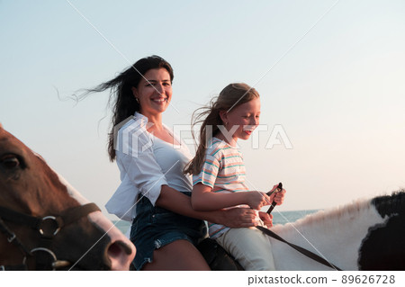 Mother and daughter enjoy riding horses together by the sea. Selective focus  89626728