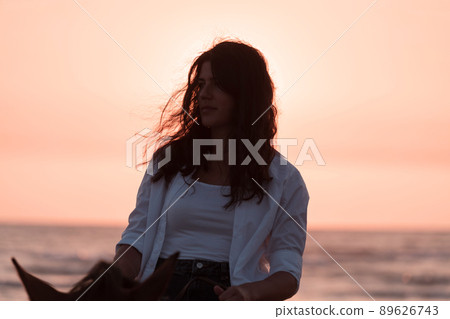 Woman in summer clothes enjoys riding a horse on a beautiful sandy beach at sunset. Selective focus Woman in summer clothes enjoys riding a horse on a beautiful sandy beach at sunset. Selective focus 89626743