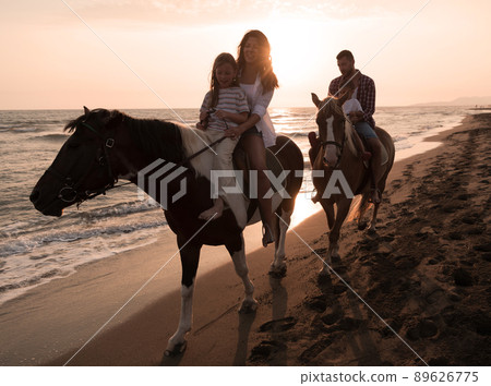 The family spends time with their children while riding horses together on a sandy beach. Selective focus The family spends time with their children while riding horses together on a sandy beach. Selective focus 89626775