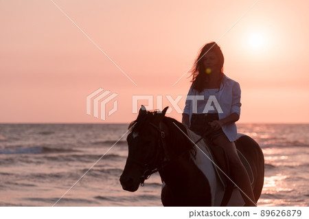 Woman in summer clothes enjoys riding a horse on a beautiful sandy beach at sunset. Selective focus  89626879