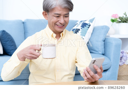 Middle-aged man using a smartphone in the living room Middle-aged man using a smartphone in the living room 89628260