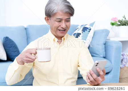 Middle-aged man using a smartphone in the living room Middle-aged man using a smartphone in the living room 89628261