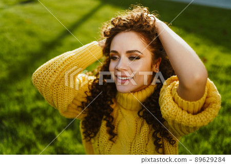 Close-up on the green bright grass girl in a bright yellow sweater raises her curly hair with her hands 89629284
