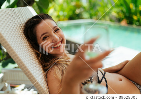 Smiling girl with beautiful teeth holds glasses stretching them into the camera in the background of the pool Smiling girl with beautiful teeth holds glasses stretching them into the camera in the background of the pool 89629303