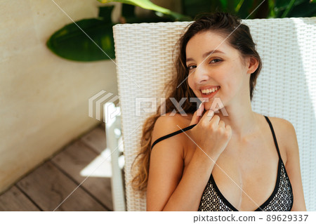 In the shisong on the veranda coquettishly adjusting the strap of the swimsuit and gently smiling sits a beautiful girl 89629337