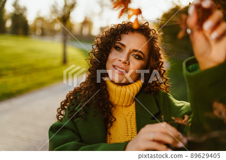 Slightly tilted sideways head looking with a slight smile and attention in the eyes of a beautiful woman in autumn clothes in the park Slightly tilted sideways head looking with a slight smile and attention in the eyes of a beautiful woman in autumn clothes in the park 89629405