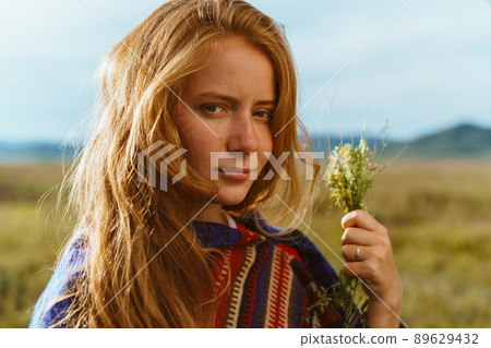 red-haired with freckles on the face of the girl flirtatiously looks into the camera holding a bouquet of wild flowers 89629432
