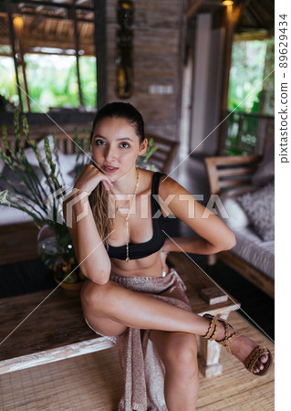 sitting on a bench in a hotel room the girl threw her foot on her leg and plunged her chin with her hand 89629434