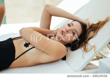 On the shisong lies a girl in a stylish swimsuit touches her hair and neck with her hand 89629436