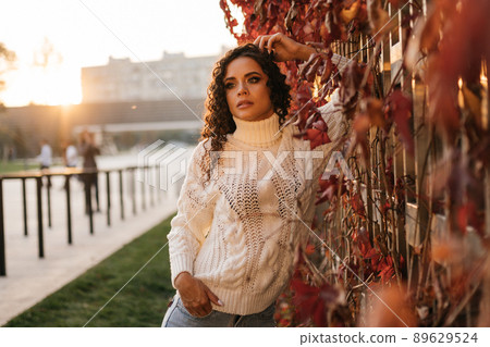 At the wall entwined with red leaves stands leaning on her elbow stylish girl dressed in the style of casual At the wall entwined with red leaves stands leaning on her elbow stylish girl dressed in the style of casual 89629524