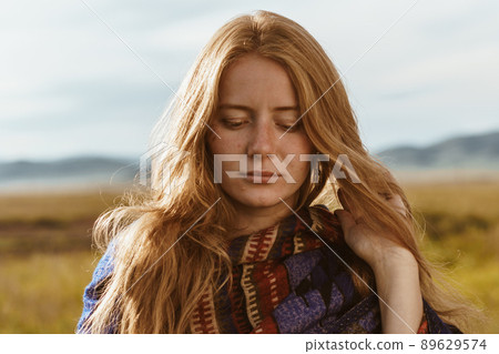 Beautiful Slavic girl without makeup with red hair drooping eyes looking down standing in the steppe against the backdrop of hills Beautiful Slavic girl without makeup with red hair drooping eyes looking down standing in the steppe against the backdrop of hills 89629574