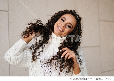Smiles and plays with her curly brunette hair with a charming white-toothed smile. close-up 89629579