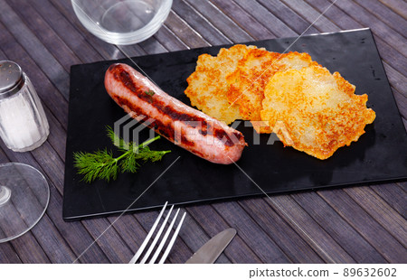 Fried potato pancakes on black slate board with grilled sausage Fried potato pancakes on black slate board with grilled sausage 89632602
