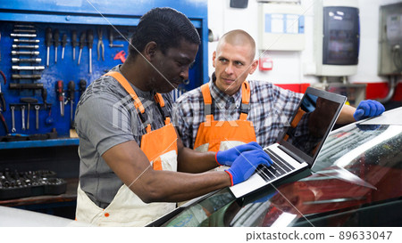 Two auto mechanics diagnosing car engine with laptop Two auto mechanics diagnosing car engine with laptop 89633047