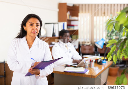 Polite female doctor filling out medical form at clipboard 89633073