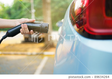 Unrecognizable Asian woman holding AC type 2 EV charging connector at EV charging station, woman preparing an EV - electric vehicle charging connector for recharge a vehicle. Unrecognizable Asian woman holding AC type 2 EV charging connector at EV charging station, woman preparing an EV - electric vehicle charging connector for recharge a vehicle. 89634264