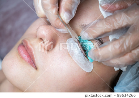 The master combs the eyelashes of a woman with a fish applicator. The master combs the eyelashes of a woman with a fish applicator. 89634266