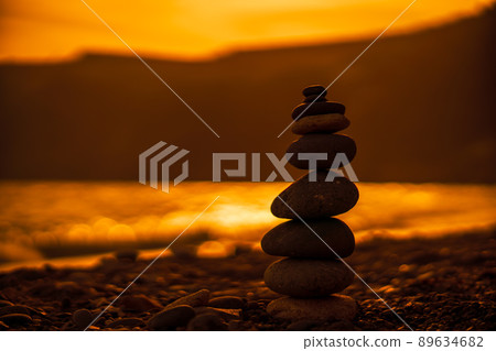 Pebble pyramid silhouette on the beach. Sunset with sea in the background. Zen stones on the sea beach concept, tranquility, balance. Selective focus 89634682