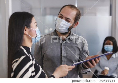 Positive and confident employer wearing protective mask while talking with job applicant about CV resume. Unemployed asian woman giving HR department manager recruiting form while in lobby area. 89635544