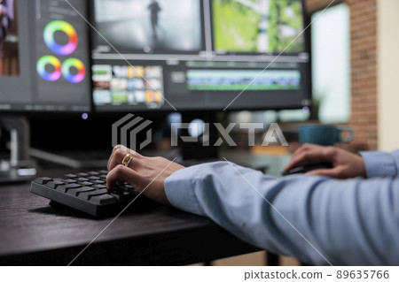 Close up shot of digital video editor sitting at multi monitor workstation desk while working on movie footage. Creative post production house videographer improving film frames visual quality. Close up shot of digital video editor sitting at multi monitor workstation desk while working on movie footage. Creative post production house videographer improving film frames visual quality. 89635766
