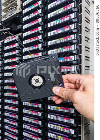 hand of a technician holding data storage magnetic tape in front of data storage array 89636566