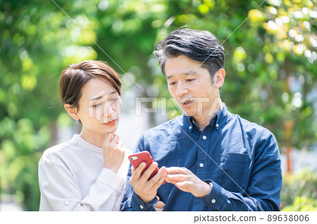 Middle couple looking at smartphone (couple, outdoor, fresh green, thinking, trouble, problem) 89638006