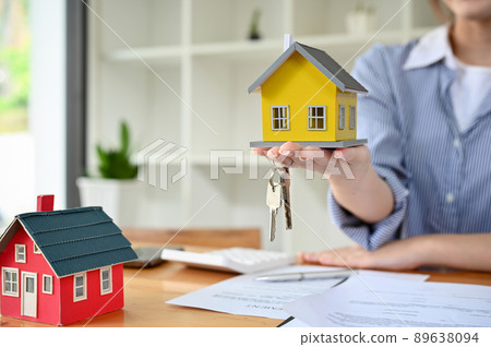 Female real estate agent showing a house model and house keys over the office desk. Female real estate agent showing a house model and house keys over the office desk. 89638094