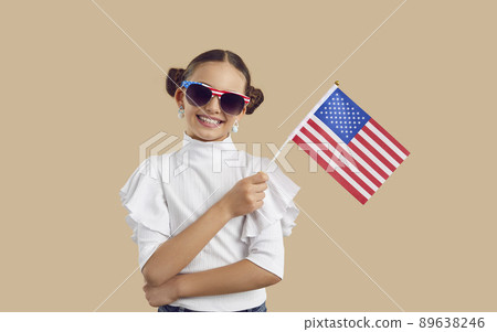 Portrait of pretty girl in sunglasses standing in studio, holding American flag and smiling Portrait of pretty girl in sunglasses standing in studio, holding American flag and smiling 89638246
