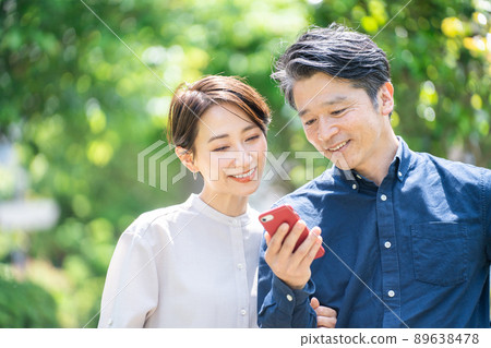 Middle-aged couple looking at a smartphone (couple, outdoor, fresh green, smile) Middle-aged couple looking at a smartphone (couple, outdoor, fresh green, smile) 89638478